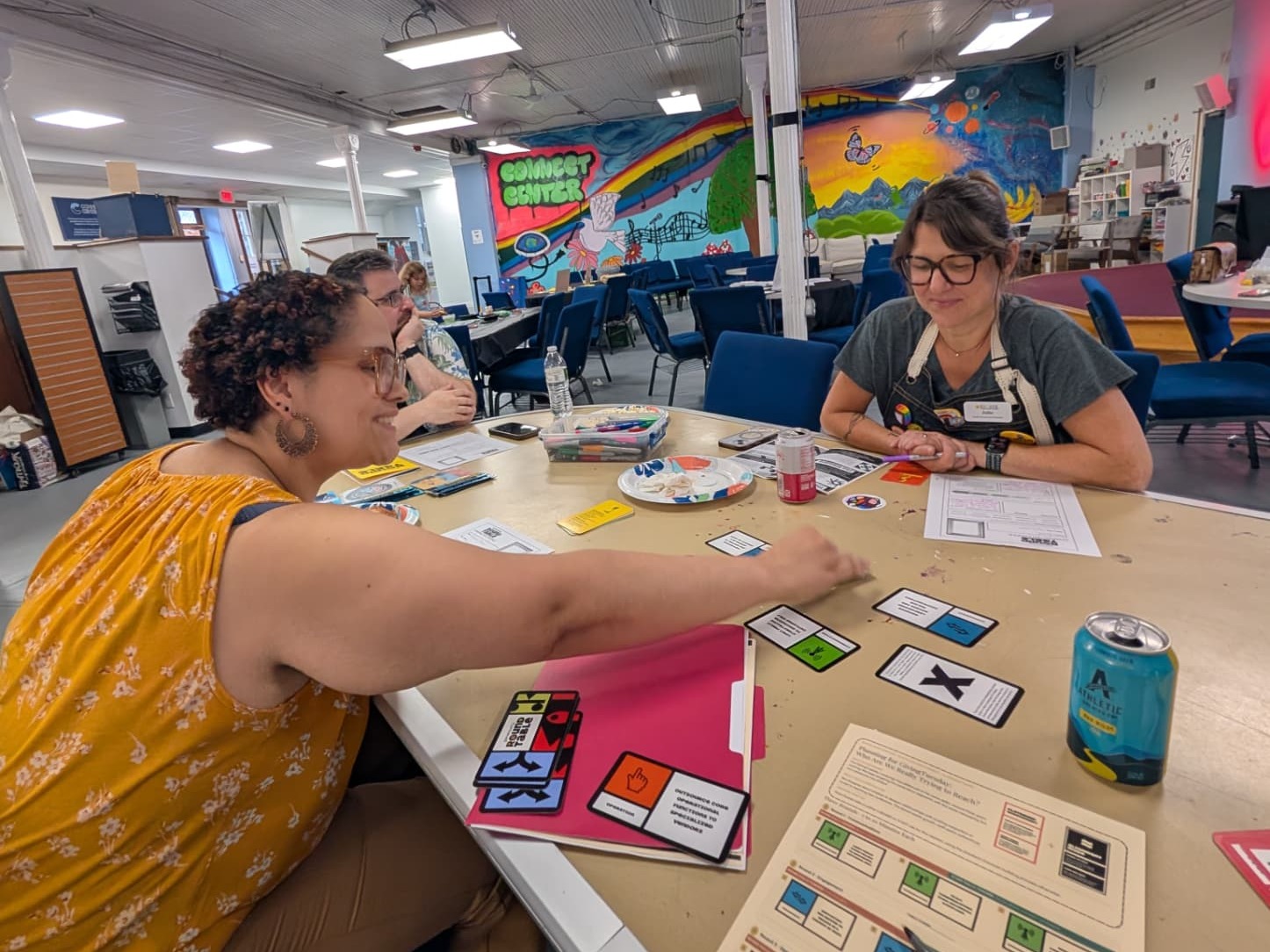 Two adults playing a generosity game at a table at the Connect Center in Cohoes, with the center's mural behind them